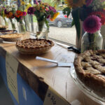 A row of fruit pies on a wooden sideboard decorated with bouquets of garden flowers.