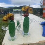 Three hand blown pickle trophies on a Cornhole board