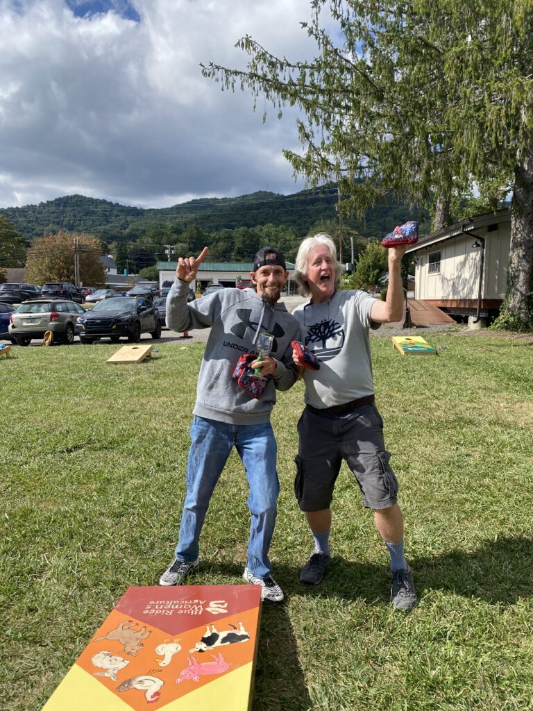 Tree Rountree and BJ McCurry posing in front of a Cornhole board with their pickle goblet trophy